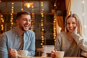 A smiling couple gazing at each other in a digital space filled with hearts and floating chat bubbles, representing the potential for reaching real connection through one conversation at a time approach.